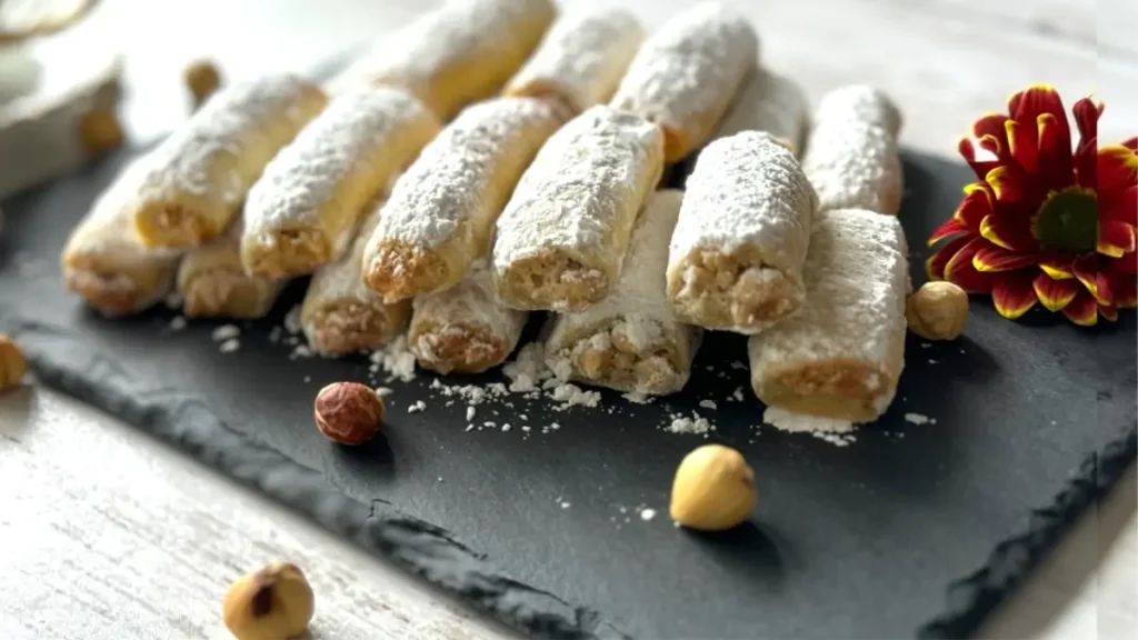أصابع البندق الهشة على طبق أبيض مع رشّة من السكر البودرة، مثالية لتقديمها مع القهوة أو الشاي.
